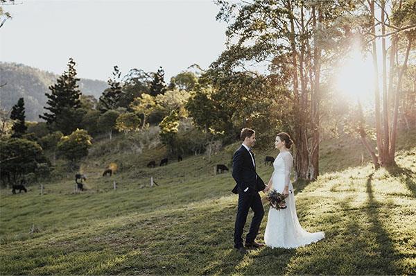 Newly married couple sntanding together in a field over looking a valley
